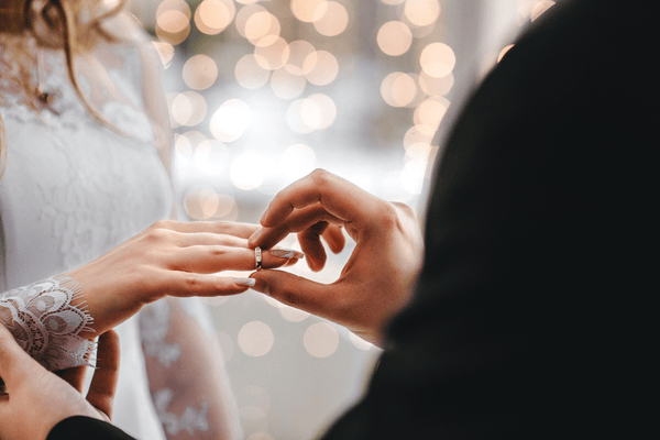 A groom slipping an eternity band onto his bride's wedding finger.