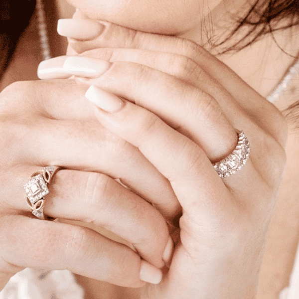 A woman's interlaced fingers with a diamond ring on each hand. Reimagined heirloom pieces form the foundation of a ring stack.