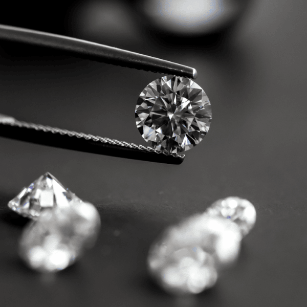 A forceps holding a round brilliant cut diamond. Select a moissanite or lab-grown diamond for your bespoke ring stack.