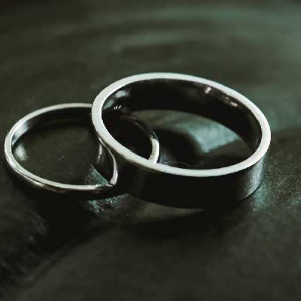 A pair of scratch proof wedding bands resting on a dark slate surface.